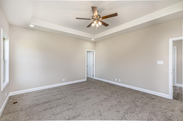 carpeted empty room featuring visible vents, baseboards, a tray ceiling, and a ceiling fan