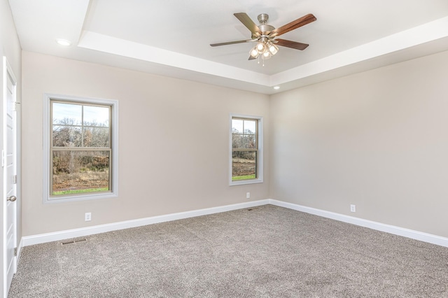 carpeted spare room featuring a tray ceiling, baseboards, visible vents, and ceiling fan