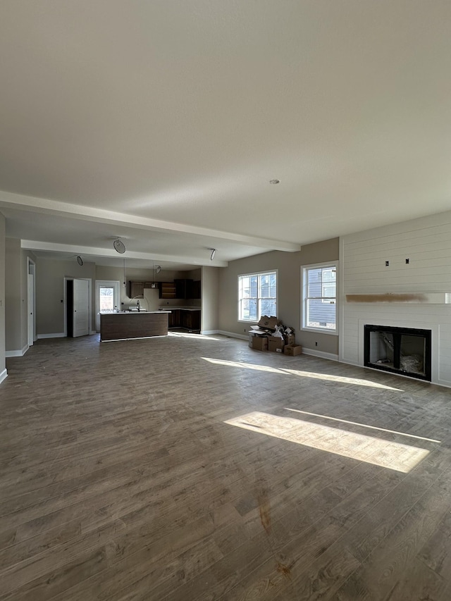 unfurnished living room with a fireplace, dark wood-type flooring, and baseboards