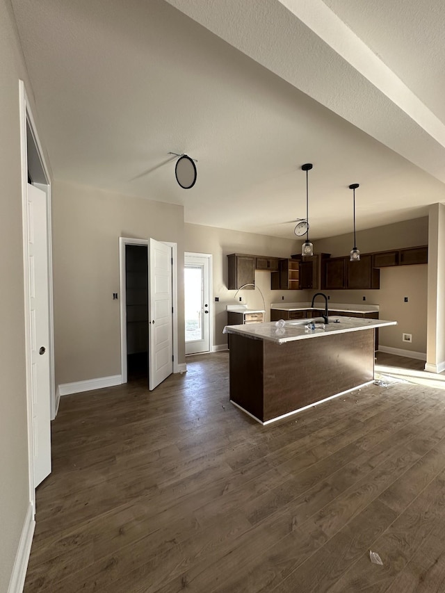 kitchen featuring decorative light fixtures, dark wood-style floors, a kitchen island with sink, and baseboards