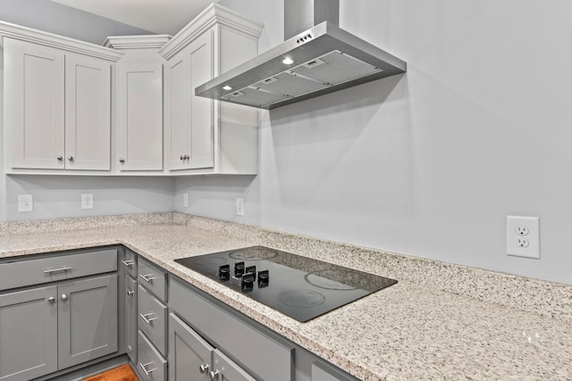 kitchen featuring black electric stovetop, wall chimney exhaust hood, gray cabinets, and light stone counters