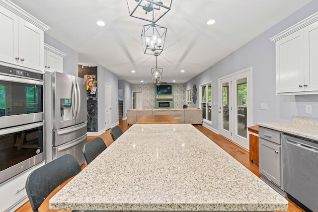 kitchen with appliances with stainless steel finishes, french doors, white cabinets, a kitchen island, and hanging light fixtures