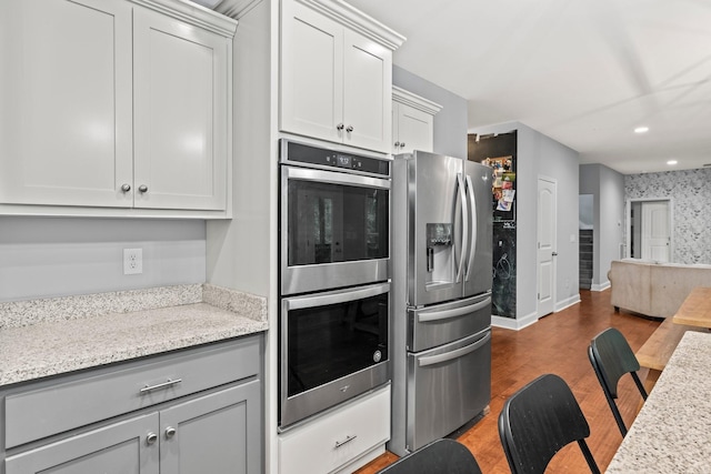 kitchen featuring dark hardwood / wood-style flooring, light stone counters, white cabinetry, and appliances with stainless steel finishes