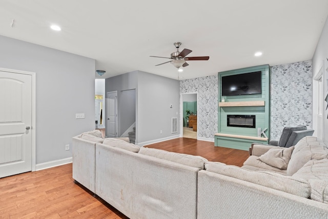 living room with hardwood / wood-style flooring, ceiling fan, and a large fireplace