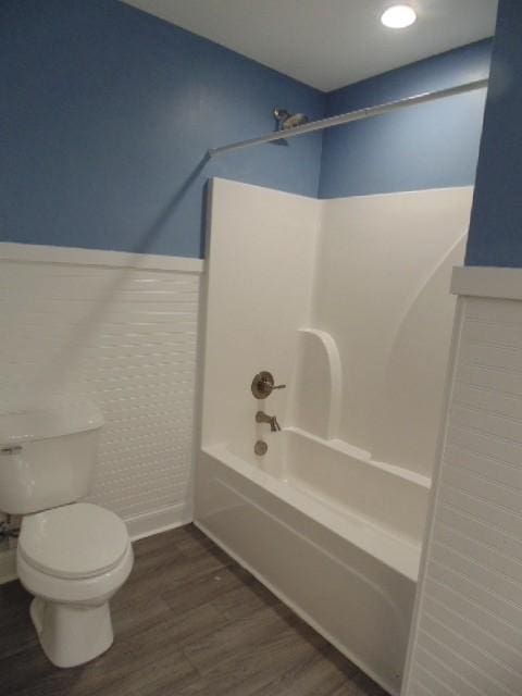 bathroom with hardwood / wood-style flooring, toilet, and washtub / shower combination