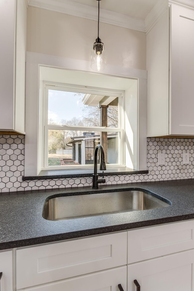 kitchen featuring decorative backsplash, ornamental molding, sink, white cabinetry, and hanging light fixtures