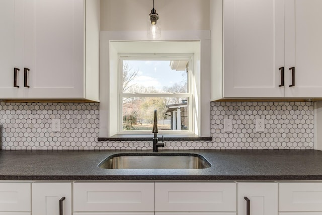 kitchen with tasteful backsplash, sink, white cabinets, and hanging light fixtures