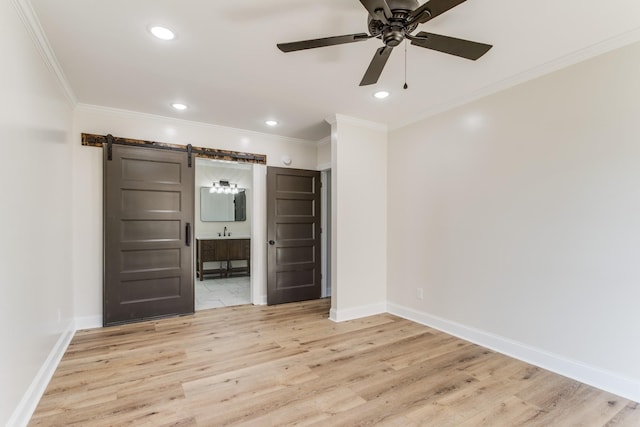 unfurnished room with ceiling fan, sink, a barn door, light hardwood / wood-style floors, and ornamental molding