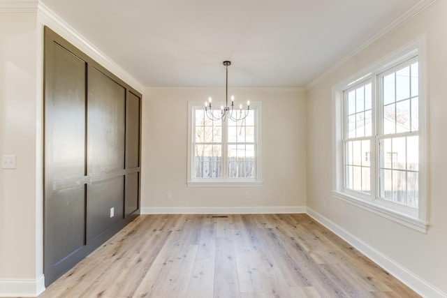 unfurnished dining area featuring a chandelier, light wood-type flooring, and crown molding