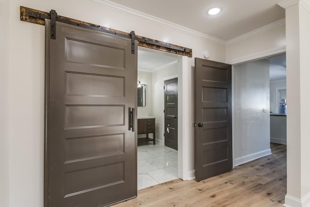 hallway with a barn door, wood-type flooring, and crown molding