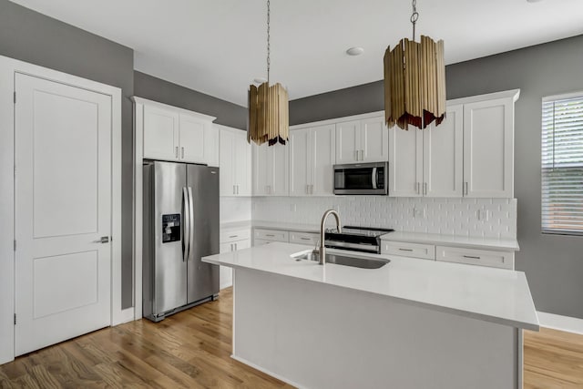 kitchen with hanging light fixtures, stainless steel appliances, white cabinetry, and a kitchen island with sink