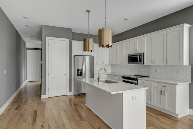 kitchen with a kitchen island with sink, hanging light fixtures, sink, white cabinetry, and stainless steel appliances