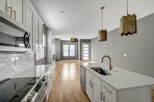 kitchen with a center island with sink, sink, decorative light fixtures, white cabinetry, and stainless steel appliances