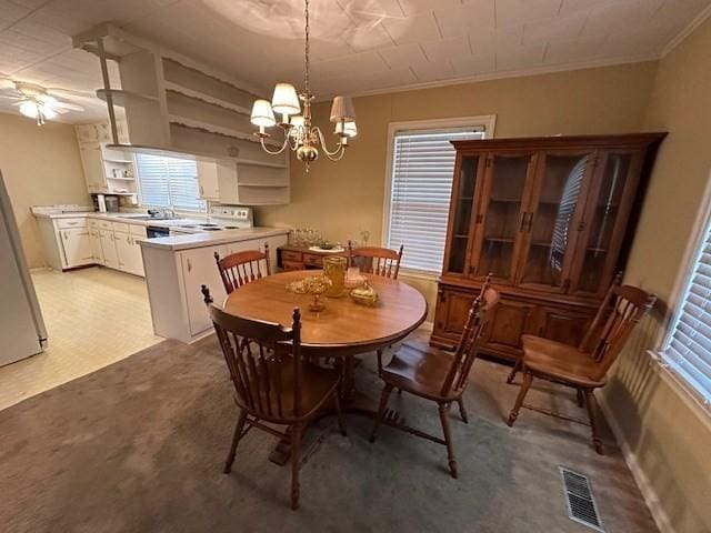 carpeted dining room with ceiling fan with notable chandelier and ornamental molding