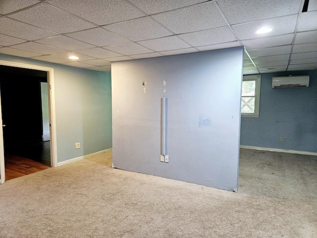 carpeted spare room featuring a wall unit AC and a drop ceiling