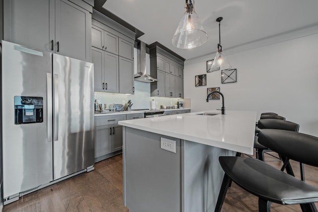 kitchen featuring sink, hanging light fixtures, stainless steel appliances, wall chimney range hood, and a kitchen island with sink