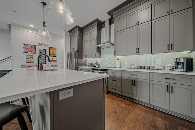 kitchen with sink, wall chimney exhaust hood, hanging light fixtures, a kitchen bar, and appliances with stainless steel finishes