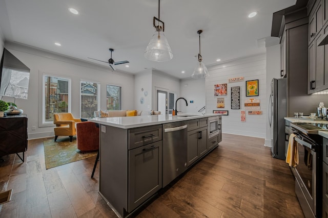 kitchen featuring appliances with stainless steel finishes, decorative light fixtures, dark hardwood / wood-style floors, and a center island with sink