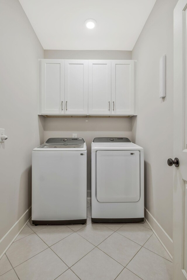 washroom featuring washing machine and clothes dryer, light tile patterned flooring, and cabinets