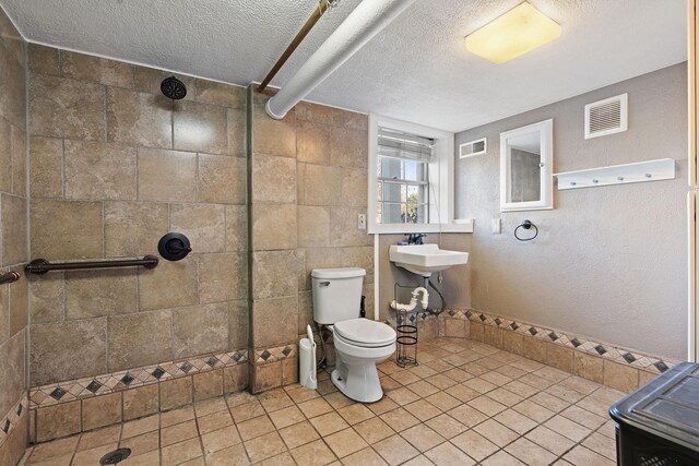 bathroom with a tile shower, sink, tile patterned floors, a textured ceiling, and toilet