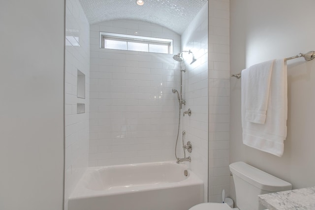 bathroom with tiled shower / bath, lofted ceiling, and toilet