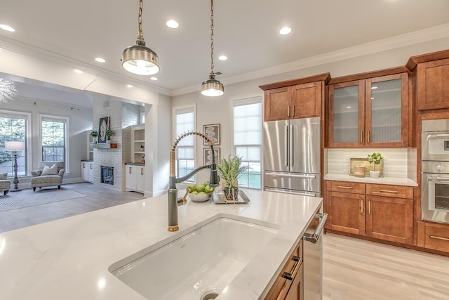 kitchen with decorative light fixtures, sink, stainless steel appliances, crown molding, and light stone countertops