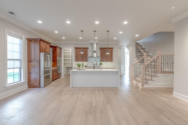 kitchen with sink, high end fridge, a kitchen island with sink, light hardwood / wood-style floors, and decorative light fixtures