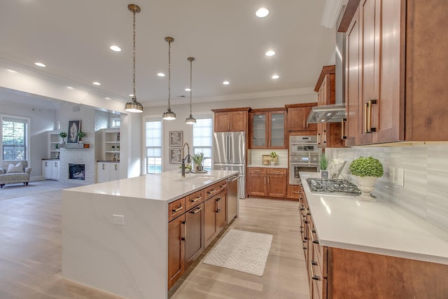 kitchen featuring sink, decorative light fixtures, a large island with sink, appliances with stainless steel finishes, and wall chimney range hood