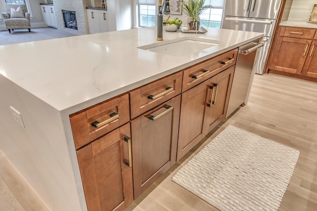 kitchen with sink, a brick fireplace, fridge, dishwasher, and light hardwood / wood-style floors