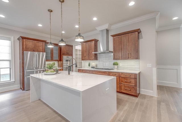 kitchen featuring appliances with stainless steel finishes, pendant lighting, wall chimney range hood, light stone countertops, and a center island with sink