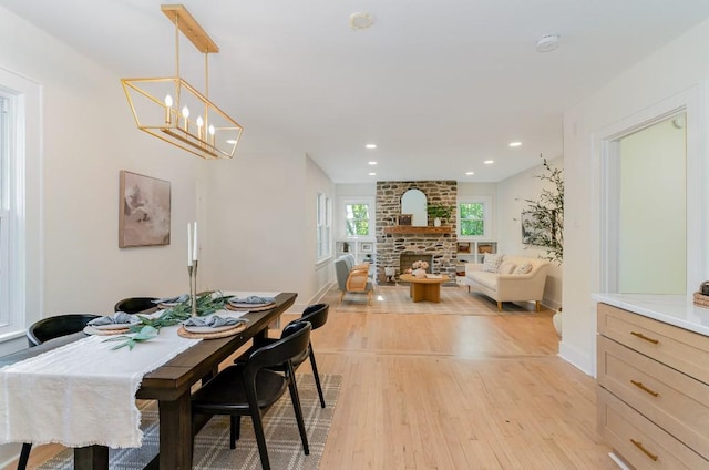 dining area featuring an inviting chandelier, light hardwood / wood-style floors, and a stone fireplace