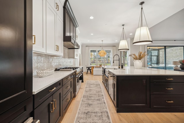 kitchen with decorative light fixtures, light wood-type flooring, white cabinetry, and stainless steel range