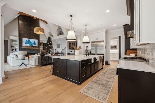 kitchen featuring white cabinets, a large fireplace, a center island with sink, and hanging light fixtures