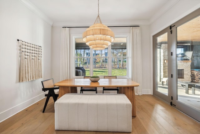 dining area with a fireplace, an inviting chandelier, ornamental molding, and light wood-type flooring