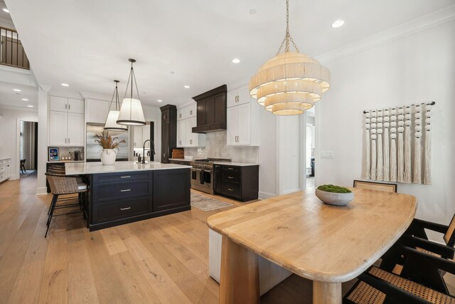 kitchen with a center island with sink, decorative light fixtures, high quality appliances, and light wood-type flooring