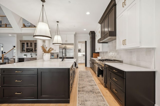 kitchen featuring a large island with sink, high quality appliances, white cabinets, and hanging light fixtures