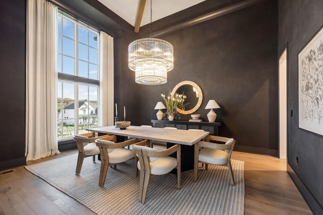 dining area with a chandelier, wood-type flooring, a healthy amount of sunlight, and a high ceiling