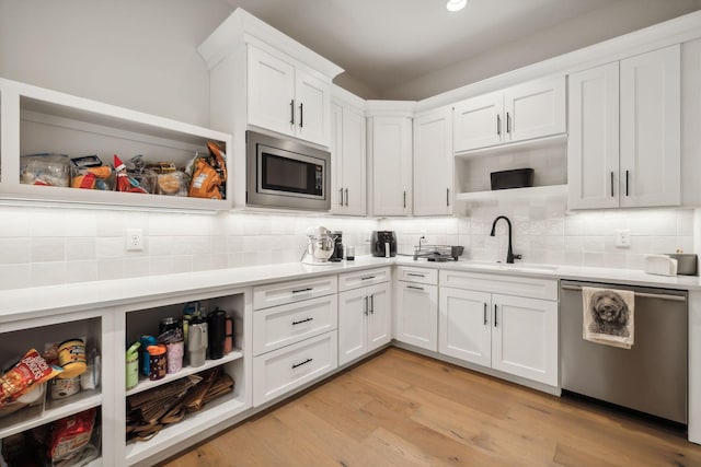 kitchen with sink, stainless steel appliances, backsplash, light hardwood / wood-style floors, and white cabinets