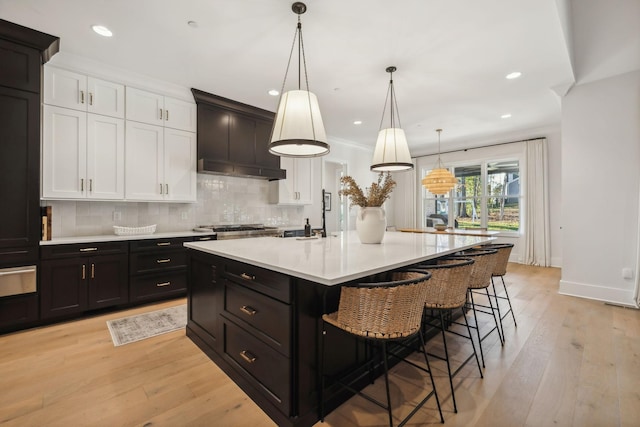 kitchen featuring hanging light fixtures, a breakfast bar area, a kitchen island with sink, white cabinets, and light wood-type flooring