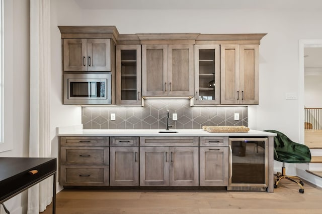 kitchen with stainless steel microwave, sink, wine cooler, tasteful backsplash, and light hardwood / wood-style floors