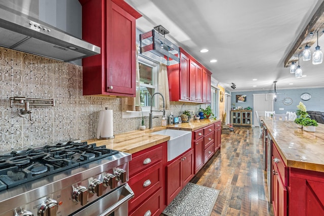 kitchen featuring stainless steel gas range oven, butcher block counters, wall chimney range hood, backsplash, and sink