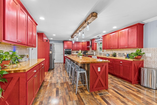 kitchen with wall chimney exhaust hood, a center island, butcher block countertops, dark hardwood / wood-style flooring, and appliances with stainless steel finishes