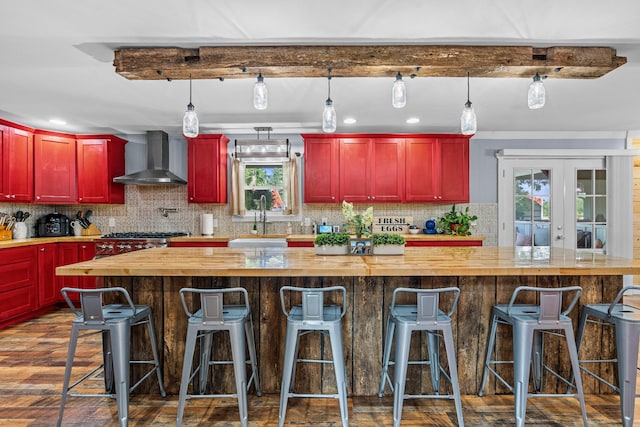 kitchen featuring pendant lighting, wall chimney range hood, a kitchen bar, a kitchen island, and sink