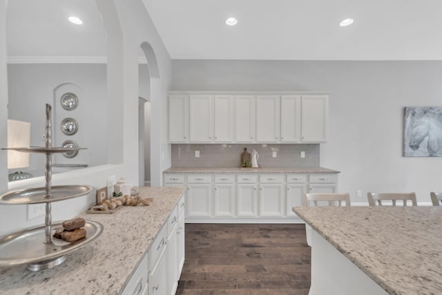 kitchen featuring white cabinets, dark hardwood / wood-style floors, light stone countertops, ornamental molding, and tasteful backsplash