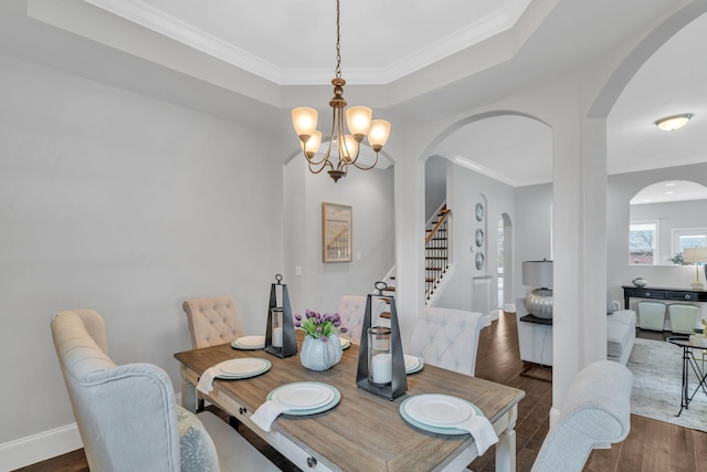 dining area featuring a raised ceiling, a chandelier, dark wood-type flooring, and ornamental molding