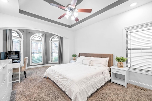 carpeted bedroom with ceiling fan and a tray ceiling