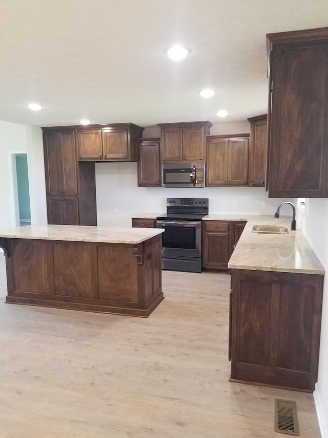 kitchen featuring sink, range with electric stovetop, dark brown cabinets, a kitchen island, and light wood-type flooring