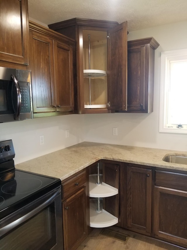 kitchen with electric range, sink, light stone countertops, and dark brown cabinets