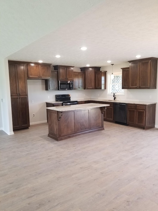 kitchen with pendant lighting, black appliances, a kitchen breakfast bar, sink, and light hardwood / wood-style flooring