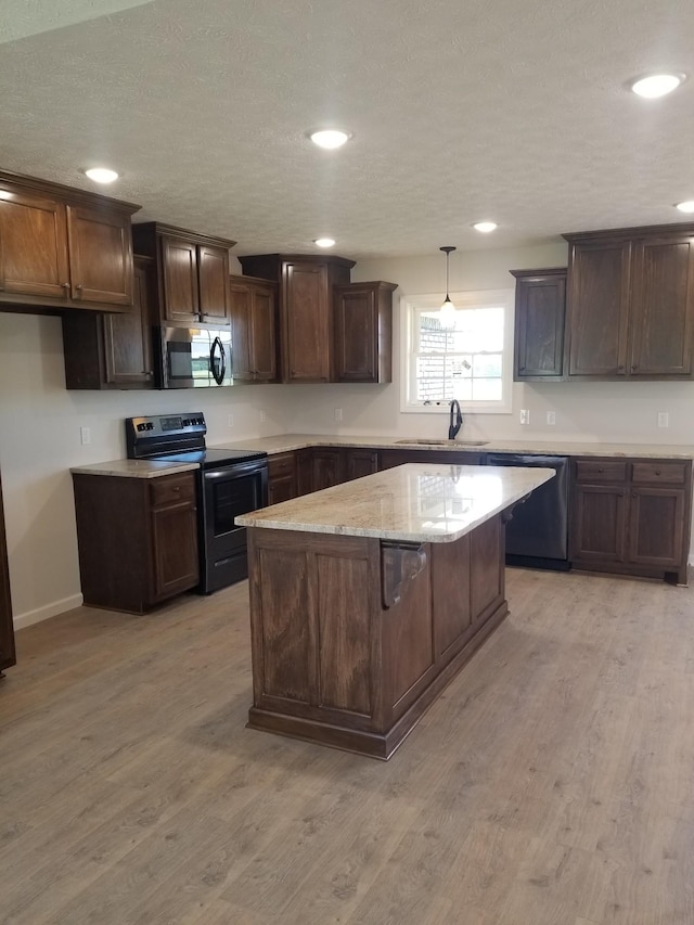 kitchen with light wood-type flooring, stainless steel appliances, sink, a kitchen island, and hanging light fixtures